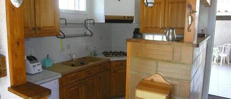 Een keuken met houten kastjes, een gasfornuis, een spoelbak en een kleine koelkast.