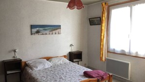 A bedroom with a wooden bed, a nightstand, a bedside table, a window with curtains, and a wall-mounted picture. - House with 3 bedrooms, 8 people, Lacanau Océan (LACANAU OCEAN)
