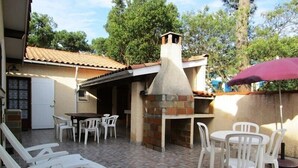 An outdoor patio with a brick oven, white plastic chairs, and a table. - House with 3 bedrooms, 8 people, Lacanau Océan (LACANAU OCEAN)