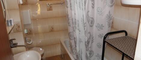 A bathroom with a bathtub, a sink, a shower curtain, and a small window.