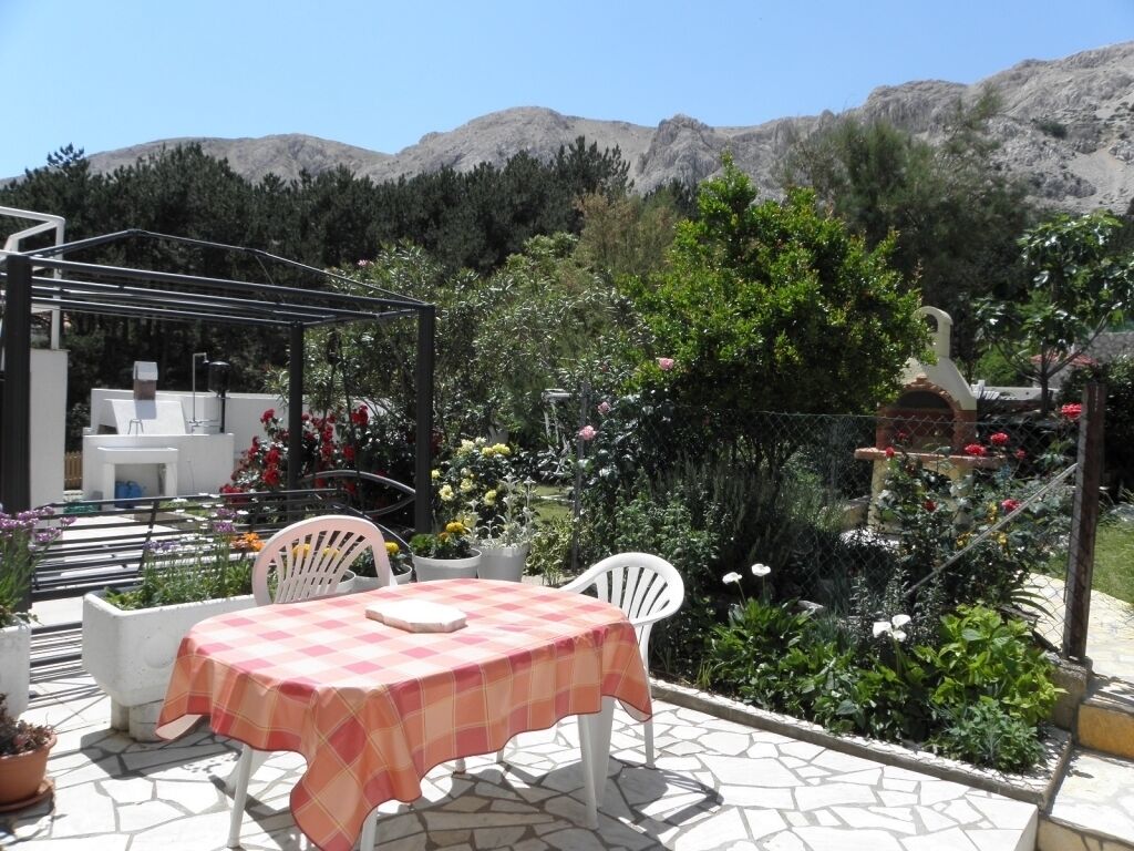 An outdoor patio with a table and chairs, surrounded by potted plants and flowers.