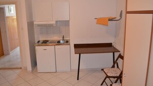 Una cocina compacta con armarios blancos, un lavamanos pequeño y una mesa de madera con una silla.