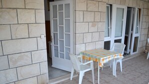 Un patio con una mesa y sillas, una puerta que da a una habitación y una ventana con persianas.