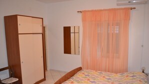 Un dormitorio con cama, armario, silla y ventana con cortinas translúcidas.