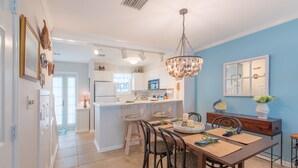A modern kitchen with white cabinets, a central island, and a dining area with a wooden table and chairs. - BELLA VITA ~ 2/1.5 located in the Truman Annex with a community pool! (Key West)
