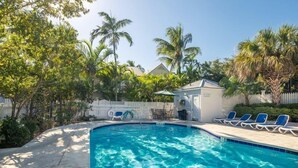 A swimming pool with lounge chairs and a small gazebo, surrounded by palm trees and a white fence. - BELLA VITA ~ 2/1.5 located in the Truman Annex with a community pool! (Key West)