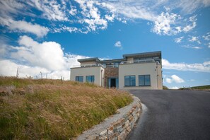 Une maison moderne à deux étages, dotée d’un mur de soutènement en pierre, de grandes fenêtres et surplombant un ciel dégagé.