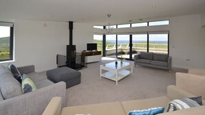 A spacious living room with a fireplace, large windows, and a view of the countryside. - Property 260 - Moyard - sleeps 8 guests  in 4 bedrooms (Connemara)