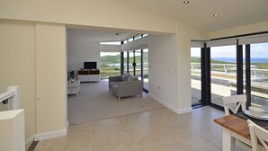 A spacious living area with a sofa, a dining table with chairs, and large windows offering a view of a landscape and a body of water. - Property 260 - Moyard - sleeps 8 guests  in 4 bedrooms (Connemara)