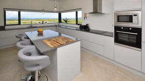 A modern kitchen with a large island, bar stools, a built-in oven, and a view of the countryside. - Property 260 - Moyard - sleeps 8 guests  in 4 bedrooms (Connemara)