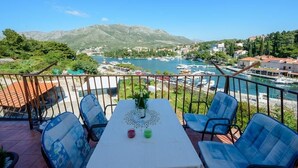 Un balcon avec une table, des chaises et une vue sur un lac, avec des bateaux et des bâtiments en arrière-plan.