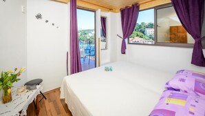 Une chambre avec un lit, une petite table sur laquelle est posé un vase, et une vue sur un balcon et des immeubles.