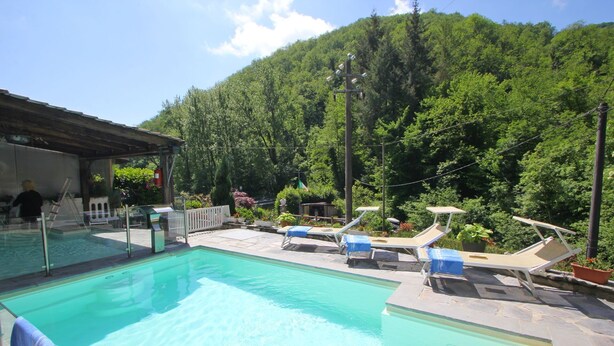 Piscina com espreguiçadeiras e área coberta, rodeada por vegetação exuberante e um cenário montanhoso.