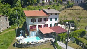 Uma casa de dois andares com piscina, cercada por vegetação e um muro de pedra.