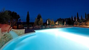A swimming pool with lounge chairs and umbrellas, surrounded by trees and a stone wall.