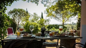 An outdoor dining table set with plates, glasses, and drinks, surrounded by chairs and a view of trees and a landscape.