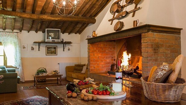 A cozy living room with a fireplace, wooden beams, a television, and a table with food and wine.