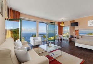 A modern hotel room with a large balcony, a sofa, a coffee table, and a bed.