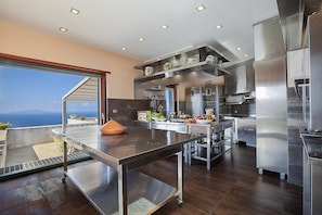 Une cuisine moderne dotée d’appareils électroménagers en acier inoxydable, d’un grand îlot central et offrant une vue sur la mer.