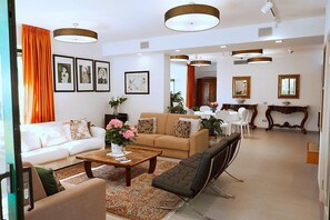 A modern living room with a sofa, coffee table, and armchair, a dining area with chairs, and a kitchen with a table and chairs. - Villa Carminia Grande: A splendid and luminous three-story villa located on the coast in front of the island of Capri, with Free WI-FI. (Massa Lubrense)