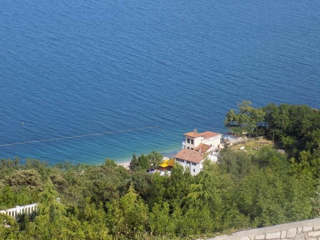 A coastal property with a white building, a beach, and dense greenery.