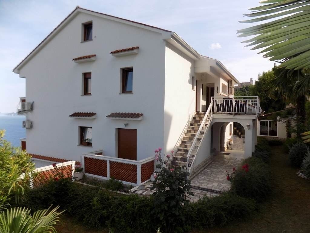 A two-story building with a balcony, a staircase, and a view of the sea.
