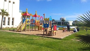 A playground with colorful play structures and a building in the background. - Very nice apartment in Savannah Beach 4210 (Sidi Rahal)