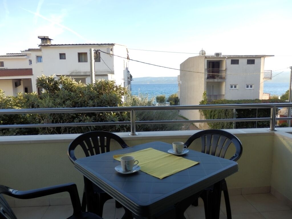 A balcony with a table and chairs, overlooking a coastal view with buildings in the background.