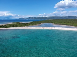 Eine Küstenlandschaft mit klarem türkisfarbenem Wasser, einem Sandstrand und einem Boot in der Ferne.