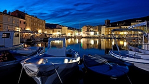 A marina at dusk with boats docked, calm water, and buildings with lights reflecting on the water. - Holiday Home in Miholaščica with Terrace, Air condition, WIFI (66-1) (Miholašcica)