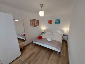 Une chambre à coucher moderne avec un lit, des tables de chevet, un miroir et des œuvres d’art accrochées au mur.