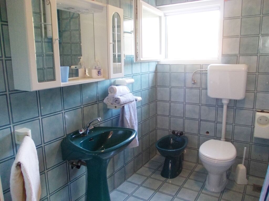 Een badkamer met een groene wastafel, een wit toilet, een bidet en een spiegel boven de wastafel.