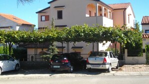 Edificio de dos pisos con techo plano y un balcón. Tres coches estacionados frente al edificio.