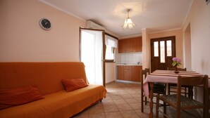 Una sala acogedora con un sofá, una mesa de comedor con sillas, una cocina al fondo y un reloj en la pared.