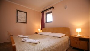Una cama bien hecha con un edredón estampado, dos mesitas de noche con lámparas, un cuadro en la pared y una ventana con cortinas.
