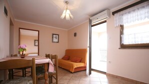 Una habitación con una mesa de comedor, sillas, un sofá, una ventana con cortinas de encaje y una lámpara en el techo.