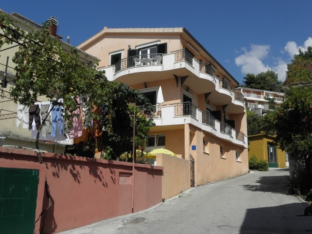 A multi-story residential building with balconies, a gated entrance, and a clear sky.