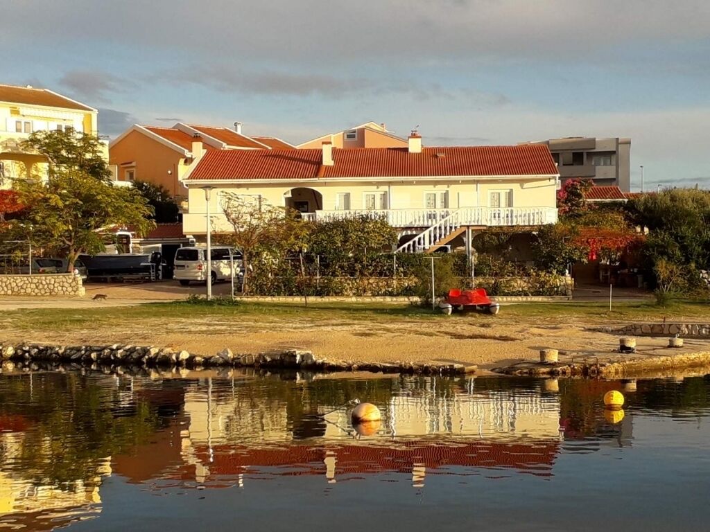A residential area with a house featuring a red roof, a small garden, and a pond with floating buoys.