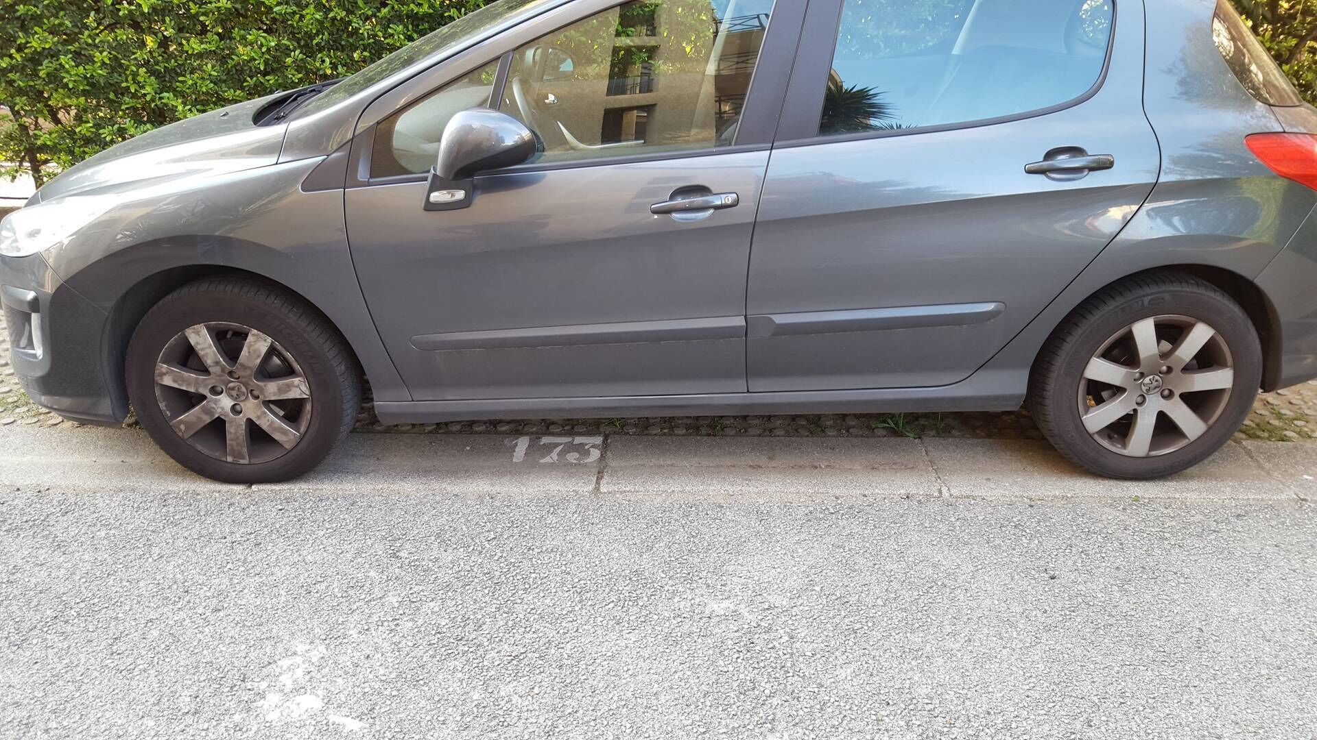 En grå hatchback parkeret på en belagt overflade, hvor nummer 175 er synligt på kantstenen.