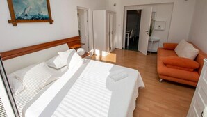A hotel room with a bed, an orange sofa, a painting on the wall, and a door leading to another room. - Apartment in Duće with Seaview, Balcony, Air condition, WIFI (4172-1) (Duce)