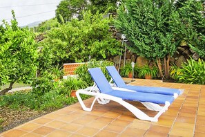 A poolside area with two blue lounge chairs and a stone wall with greenery.