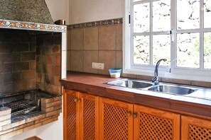 A kitchen with a built-in brick oven, wooden cabinets, a window with a view, and a sink.
