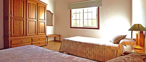 A bedroom with two beds, a wooden wardrobe, a window with blinds, and a lamp.