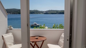 Un balcón con vistas a un lago y un barco, dos sillas blancas y una pequeña mesa de madera.