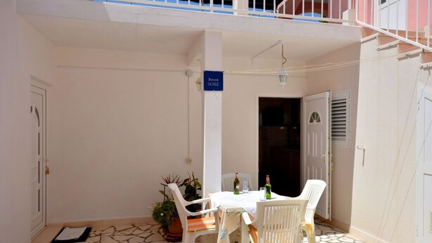 A small outdoor patio with a table and chairs, a potted plant, and a sign reading "SOBE". - Apartment in Žuljana with Seaview, Terrace, WIFI, Dishwasher (3558-2) (Žuljana)