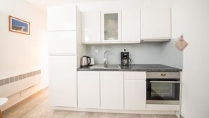 Eine kleine Küche mit weißen Schränken, einer Kaffeemaschine, einem Wasserkocher und einem Backofen.