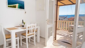 Ein Zimmer mit einem weißen Tisch und Stühlen, einem Strandbild und einem Balkon mit Meerblick.