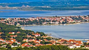 Une ville côtière aux maisons aux toits rouges, dotée d’un port de plaisance et bordée de collines.