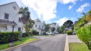 A residential street with white houses, parked cars, and lush greenery. - Large 2-bed townhouse with shared pool (Bridgetown)