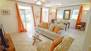 A living room with a sofa, a coffee table, and a dining area with chairs and a table. - Large 2-bed townhouse with shared pool (Bridgetown)